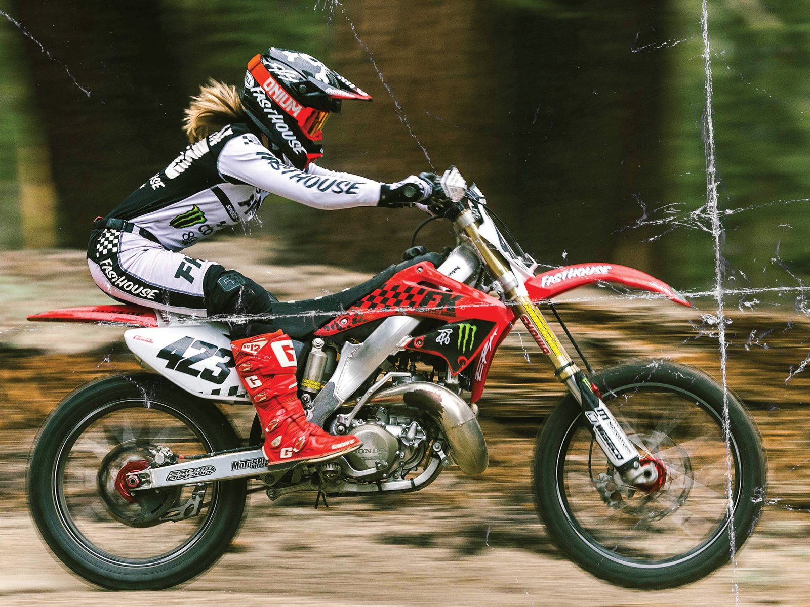 Motocross rider racing through a forest trail on a red dirt bike with distressed graphic texture overlay