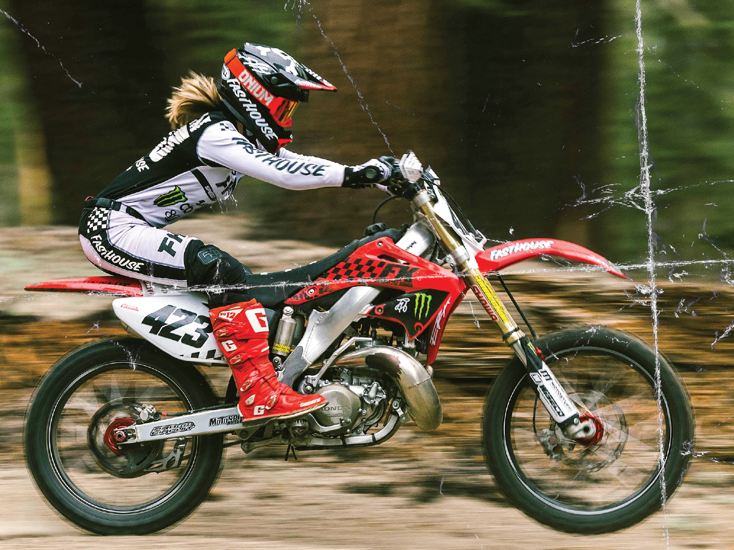 Motocross rider racing through a forest trail on a red dirt bike with distressed graphic texture overlay